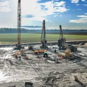 A large open area of country side with a crane and two piling rigs during construction of a circular tank that will be used to store radioactive waste in Slovenia.