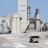 A yellow Caterpiller rigid dump truck (RDT) drives away from a huge cement factory 