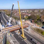 An aerial view of the new M67 St Annes Bridge under construction with a yellow crane on the near side of the bridge and a white crane on the far side.