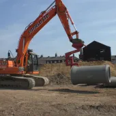 An orange excavator lifts a concrete pipe