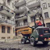 A yellow site dumper being driven in front of an urban construction site