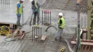 Three UK construction workers in PPE using a concrete pump to place concrete