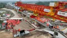 Two large groups of people in orange PPE standing on an under construction bridge deck