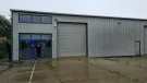 A bald man dressed in black outside a non-descript industrial estate