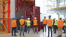 A group of people in orange PPE standing in front of red formwork panels