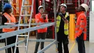 Three men in orange PPE and one in yellow inspect scaffolding