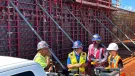 A group of construction workers in various colours of PPE stand in front of a wall of formwork