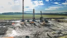 A large open area of country side with a crane and two piling rigs during construction of a circular tank that will be used to store radioactive waste in Slovenia.